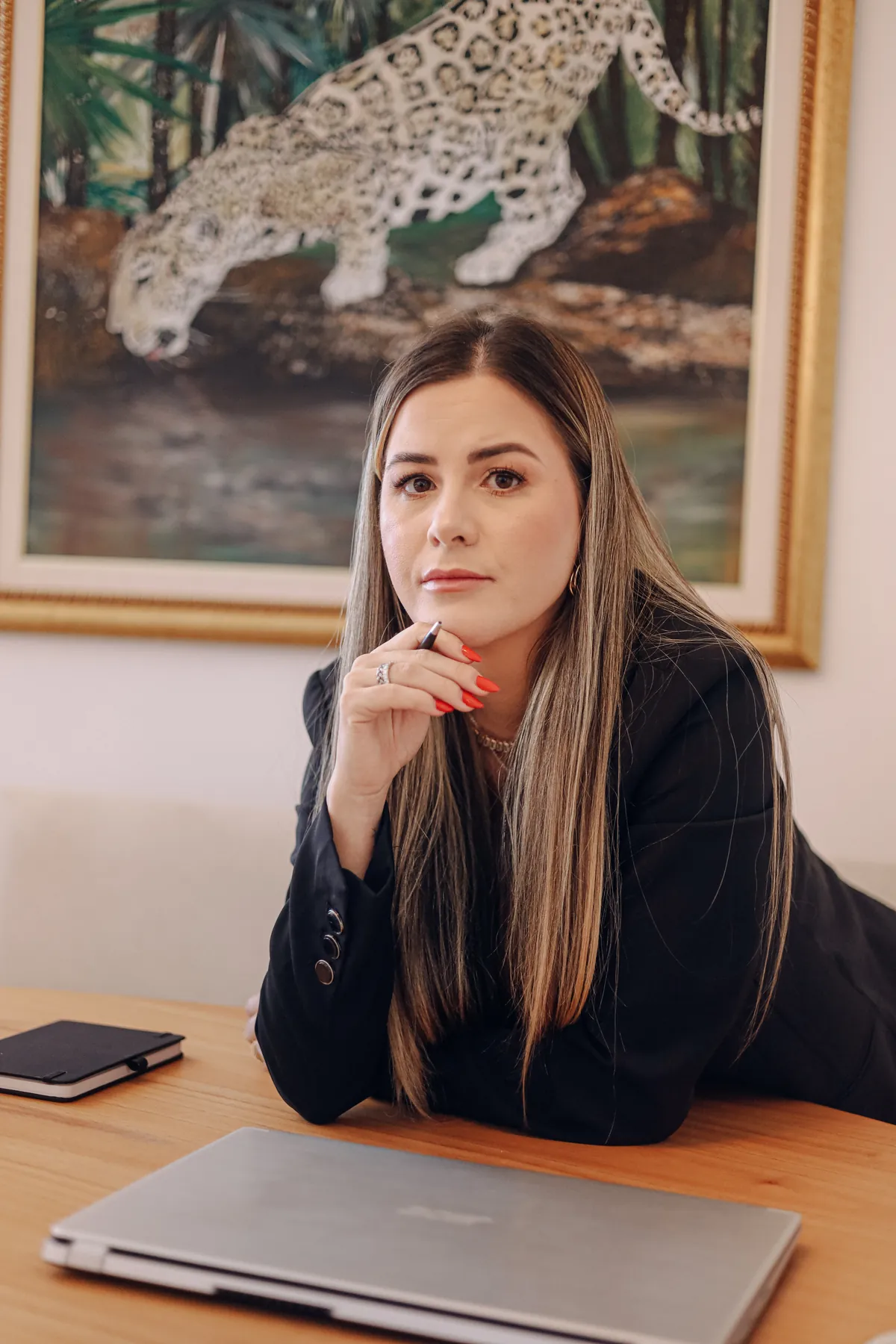 Michele Anadão à mesa do consultório, olhando para a câmera, com um quadro de onça ao fundo