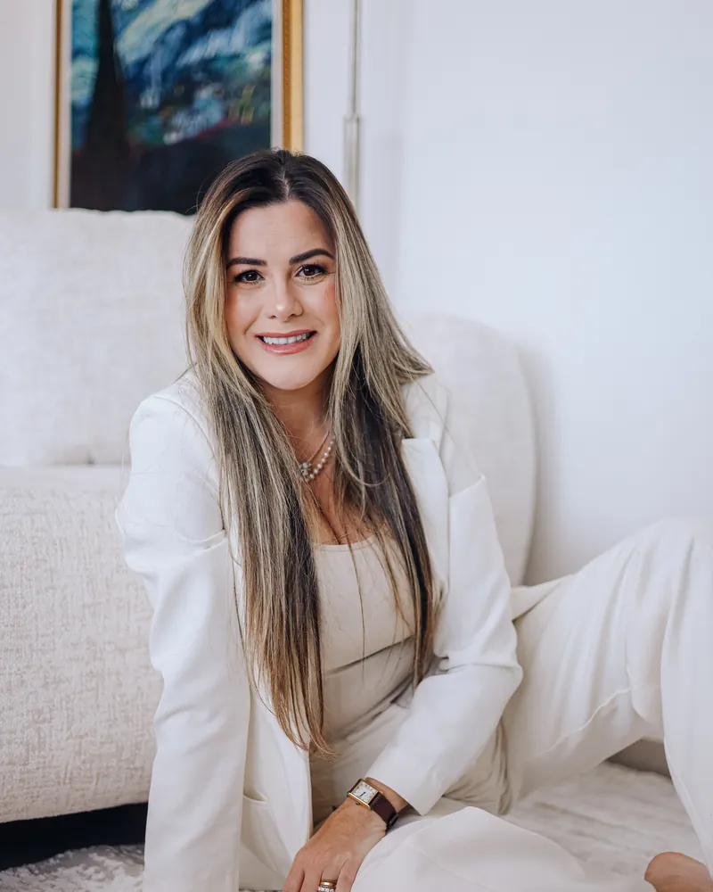 Michele Anadão sentada no chão, de roupa clara, sorrindo